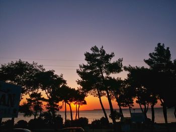 Silhouette trees by sea against clear sky during sunset