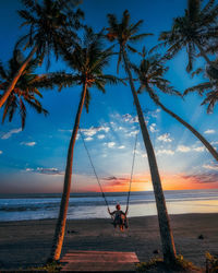 Rear view of woman on swing at beach during sunset