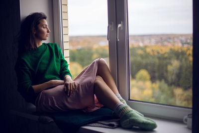 Girl sitting on the window in the green sweater in the fall