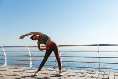 Full length of woman exercising by railing while standing against sea