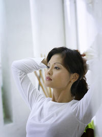 Thoughtful woman with hands behind head sitting at home