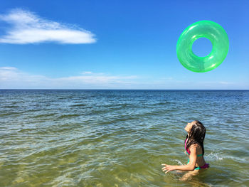 Girl playing with inflatable ring in sea against sky