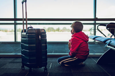 Rear view of boy sitting on window at airport