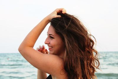 Profile view of beautiful woman smiling while standing at beach against clear sky