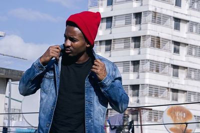 Young man looking away while standing against wall
