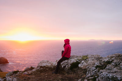 Side view of woman standing on rock against sky during sunset