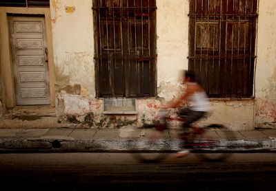 Blurred motion of woman cycling against building 