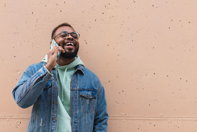 Young man using phone while standing against wall