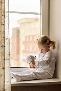 Full length of girl with stuffed toy sitting by window