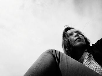 Low angle view of young woman sitting against cloudy sky