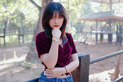 Portrait of beautiful woman with hand on chin standing against trees in park