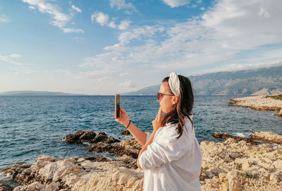 Side view of young woman taking photos on beach. summer vacation, travel, tourism, lifestyle.