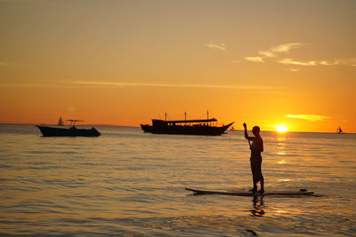 Silhouette man standing on sea against sky during sunset