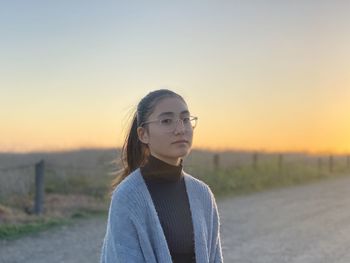 Portrait of young woman standing on land against sky during sunset