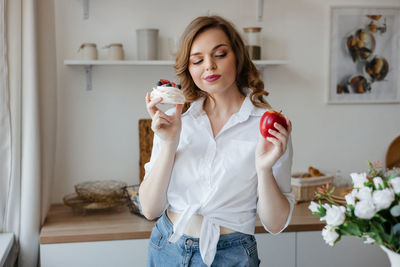 Girl holding a cake in one hand and an apple in the other in the kitchen