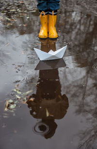 Boy standing in front of paper boat in puddle