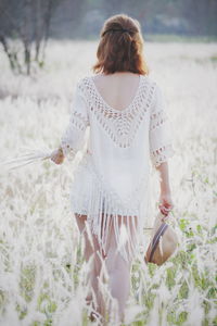 Rear view of woman holding sun hat walking on field