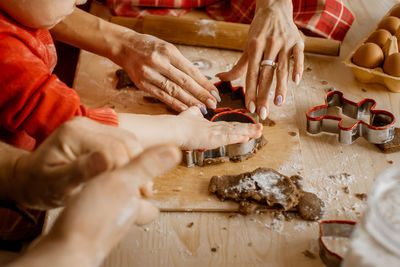 Side close up view of family member's hands cutting out different christmas shapes out of raw dough 