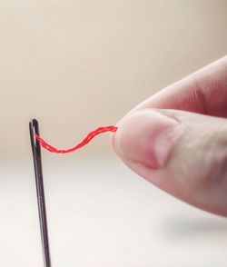 Close-up of hands threading sewing needle against white background