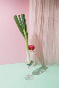 Spring onion and radish stand in a champagne glass on a pastel pink and mint background. still life