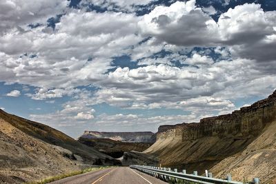 Empty road leading towards rocky mountains against cloudy sky
