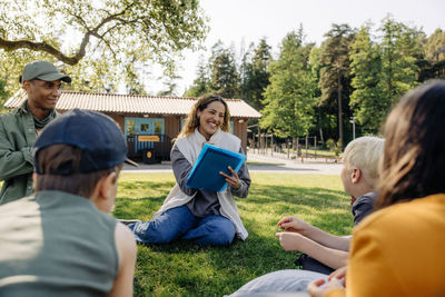 Happy female counselor doing activities with kids while sitting on grass at summer camp