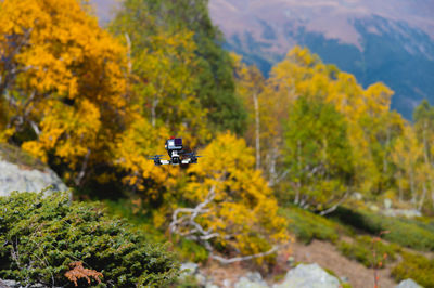 A self-assembled drone quadcopter hangs in the air against the backdrop of a mountainous open area