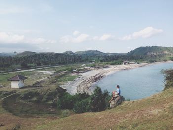 High angle view of thoughtful man sitting on rock by lake against sky