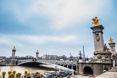 Statue of bridge over river against cloudy sky