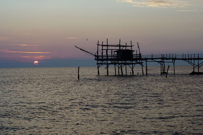 Silhouette pier over sea against sky during sunset