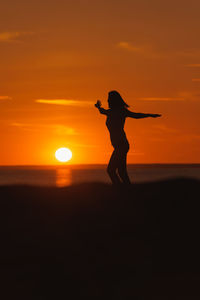 Silhouette woman standing on beach against sky during sunset