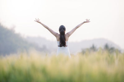 Rear view of carefree woman with arms raised standing on field against sky