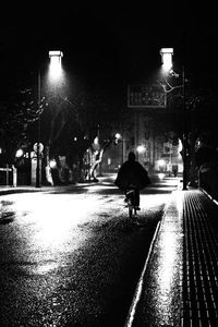 Silhouette man walking on wet illuminated road against sky at night