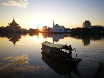 Man rowing boat in lake against sky during sunset