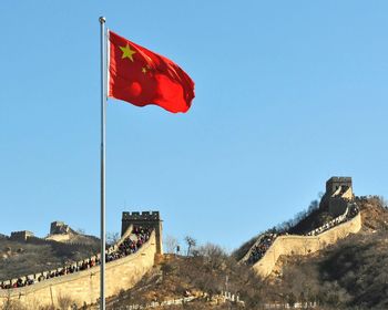 People at great wall of china by chinese flag against clear sky