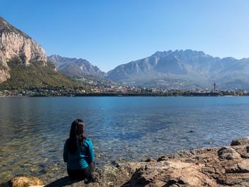 Rear view of woman looking at lake by mountains against clear sky