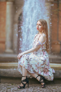 Side view of beautiful young woman sitting against fountain in city