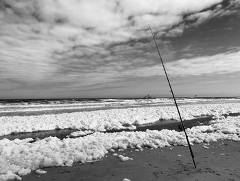 A foaming sea with a fishing rod on the beach