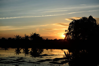 Silhouette trees by lake against romantic sky at sunset