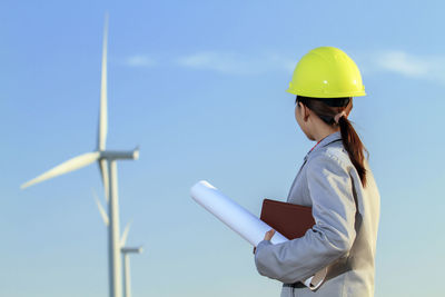 Engineer holding blueprint against sky