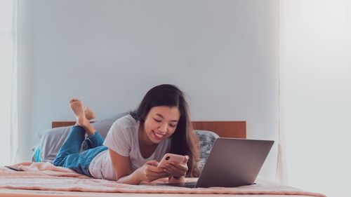 Young woman using mobile phone while sitting on bed