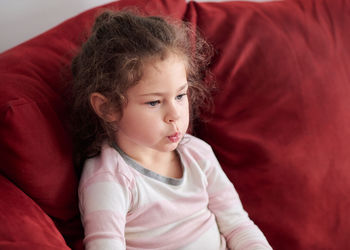 Portrait of a young girl in pajamas sitting on the couch and making faces while watching tv