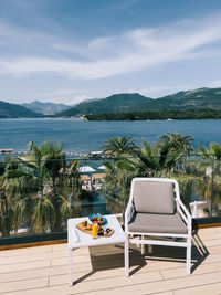 Empty chairs and table by sea against sky