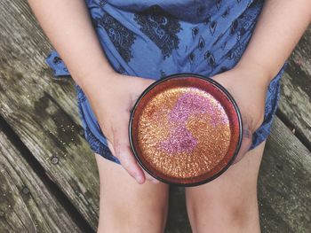 Midsection of woman holding glitter while sitting on wood