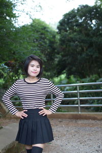 Portrait of smiling young woman standing on field against trees in forest