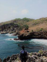 Rear view of man with backpack standing at beach against sky