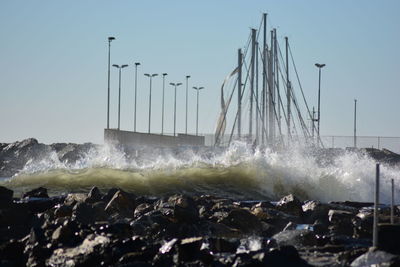Waves splashing on rocks against clear sky