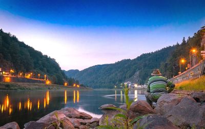 Rear view of man sitting by lake on rock