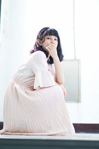 Midsection of woman sitting against white wall