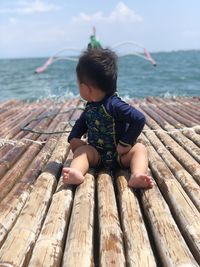 Boy sitting on wood against sea